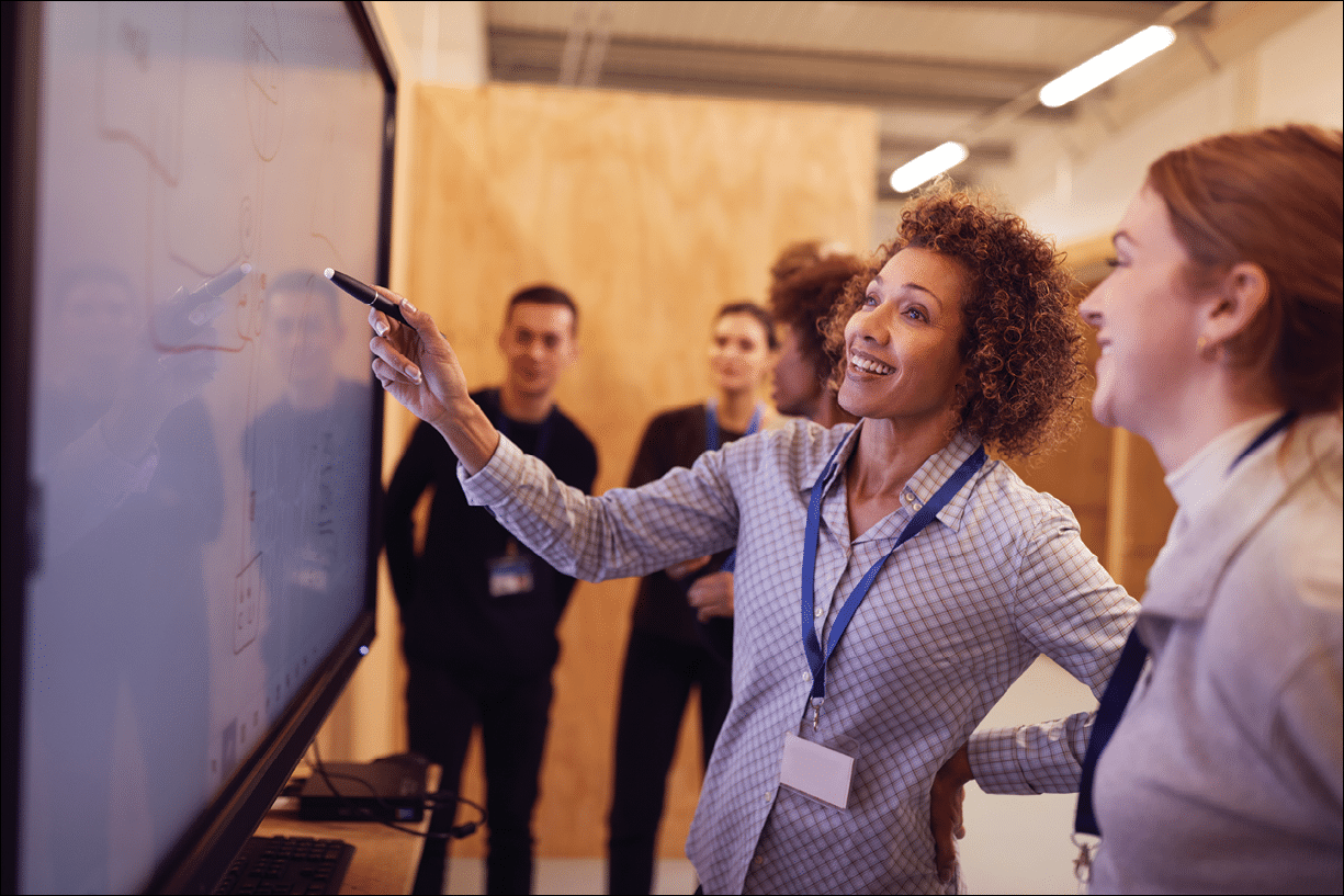 Tutor With Trainee Electricians Studying For Apprenticeship Looking At Wiring Diagram On Screen