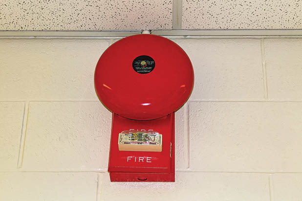 A red fire alarm hanging on a white brick wall. fire alarm on the wall of shopping center.