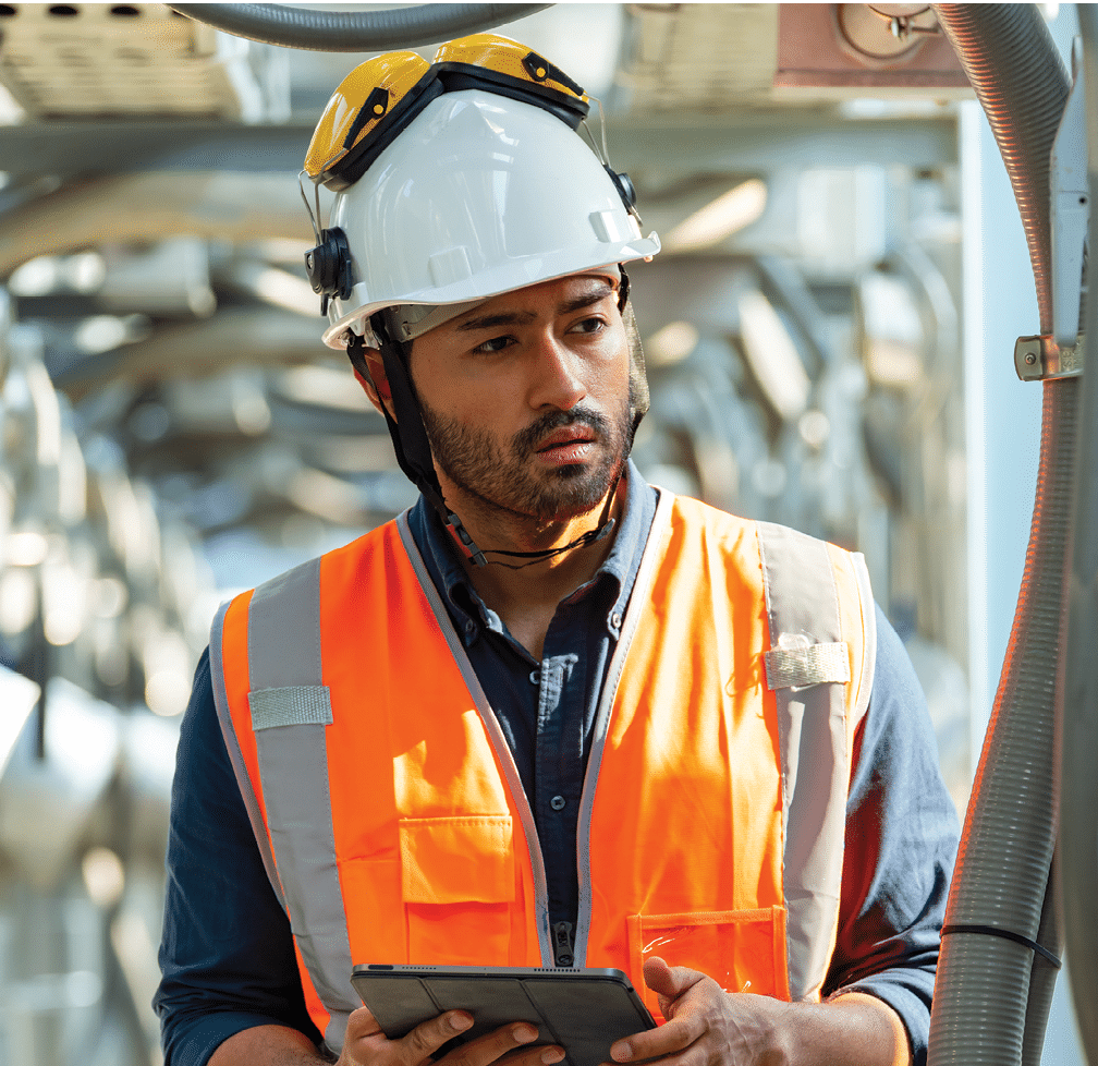 Professional Asian man engineer in safety uniform working on digital tablet at outdoor construction site rooftop. Industrial technician worker maintenance checking building exterior air HVAC systems.