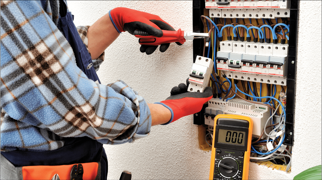 Young electrician technician introduces the electric cable into the clamp of the magnetothermic switch with an insulated clamp