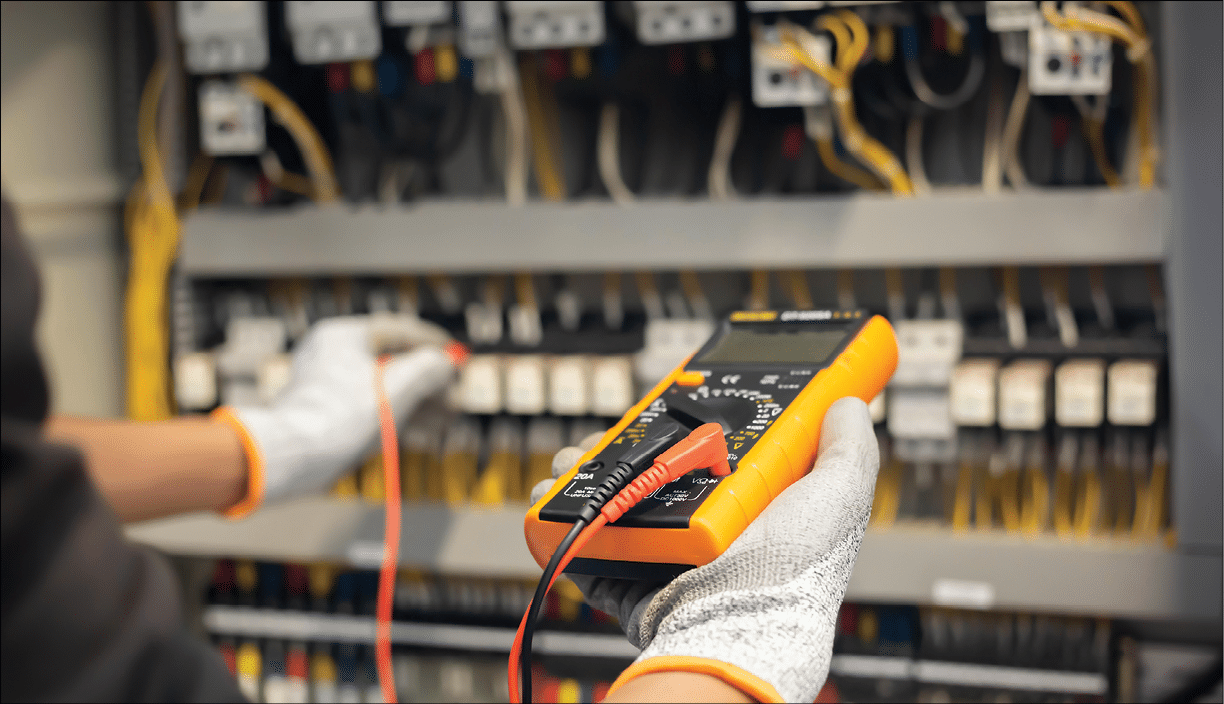 Electrician engineer uses a multimeter to test the electrical installation and power line current in an electrical system control cabinet.