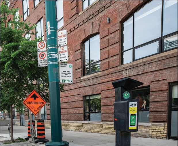 Solar powered paid parking station on the side of the street in Toronto, Ontario, Canada next to no parking signs and a construction sign in front of a brick building