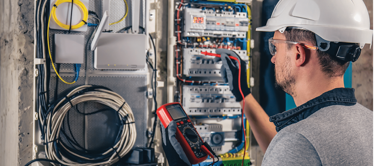 Man, an electrical technician working in a switchboard with fuses. Installation and connection of electrical equipment. Professional uses a tablet.