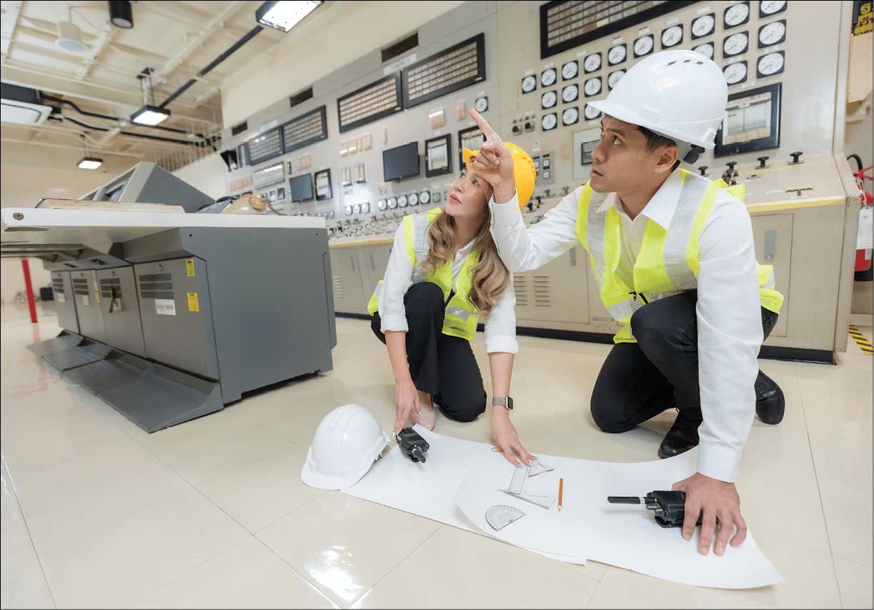 Asian male and female engineers Points to the machine circuit boards that produce energy in the world's industrial power plants. Do design work with a blueprint. Wear a safety helmet and vest.