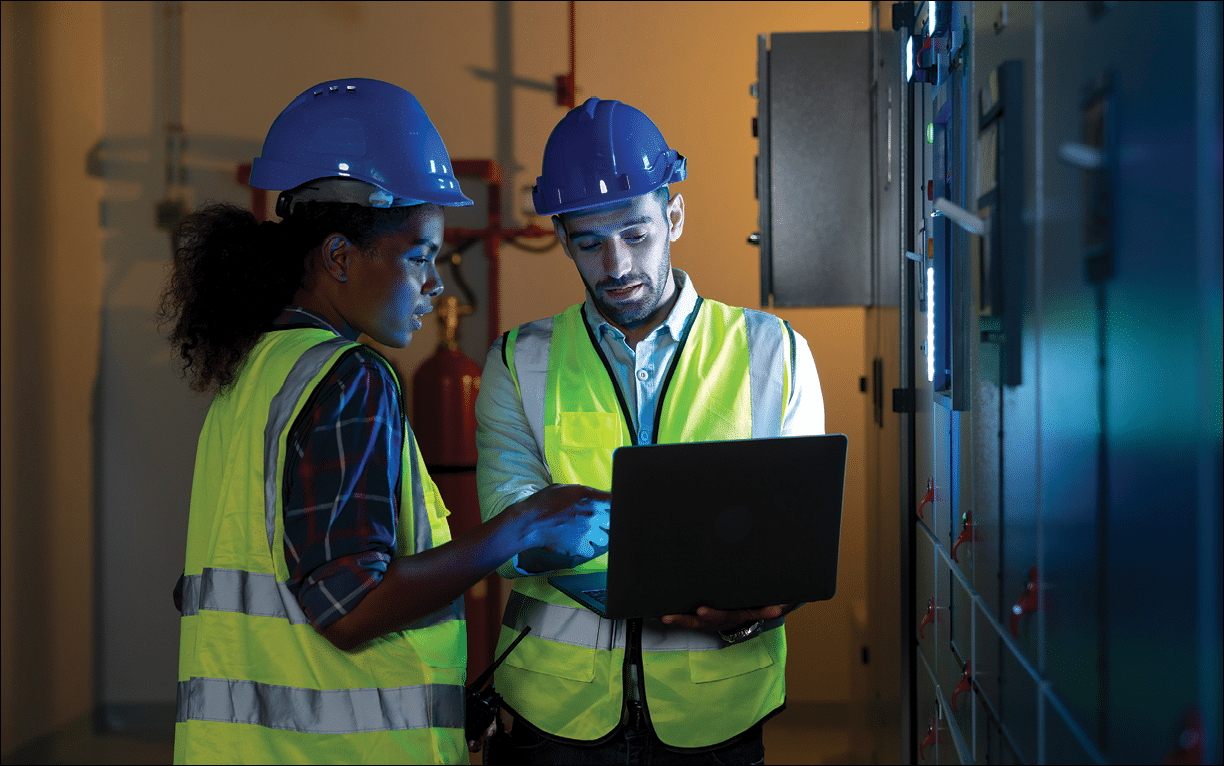 Electrical engineer use laptop to inspection and testing of electrical system in control room. Electrician and technician working night shifts at distribution board. Multi-Ethnic Blue-collar worker.