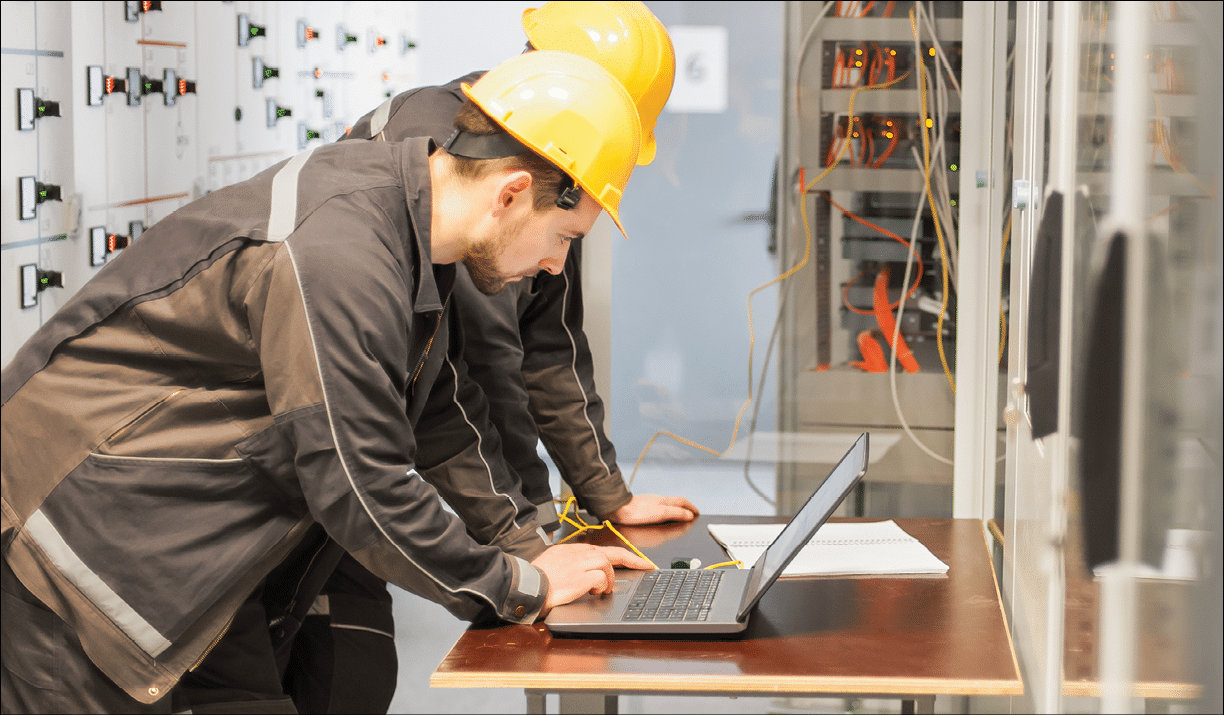 Two maintenance engineers inspect relay protection system with laptop computer. Bay control unit. Medium voltage switchgear