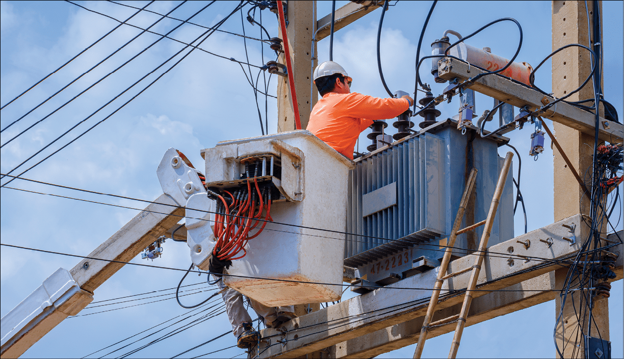 Electrician in bucket of articulated boom lift is repairing electrical transmission on power poles against blue sky background