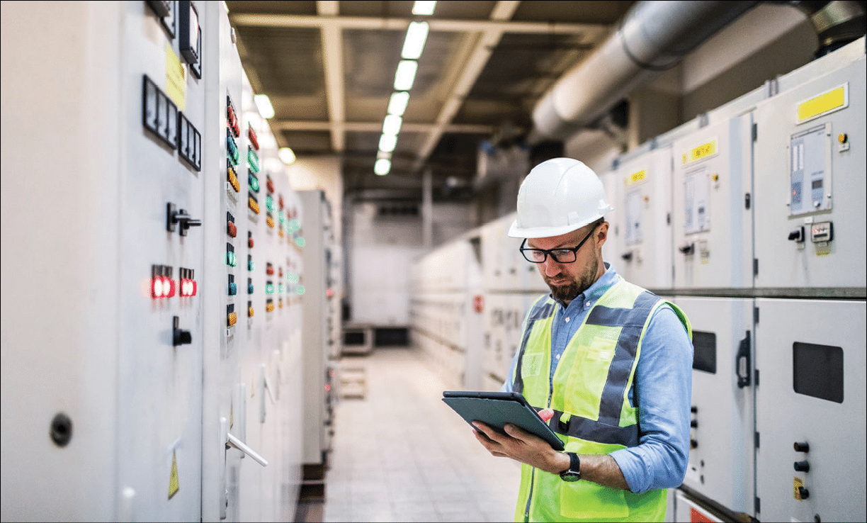 A man in a yellow vest is looking at a tablet. Description generated by AI