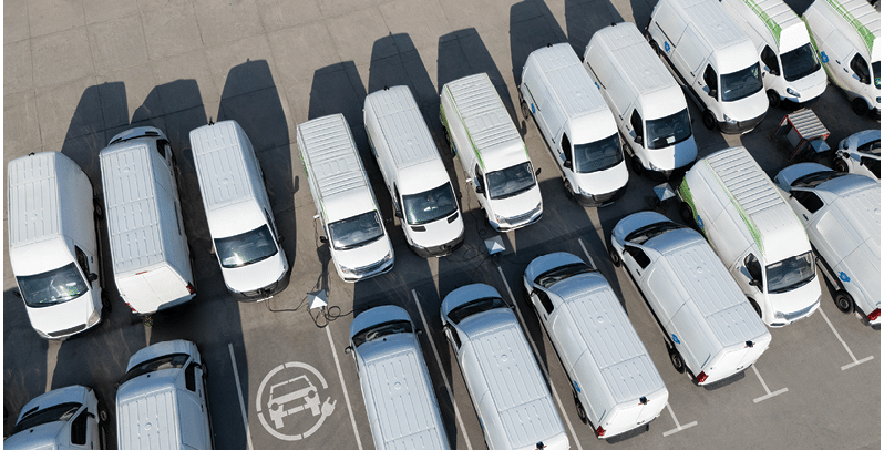 Rows of white electric delivery vans at charging stations for electric vehicles.