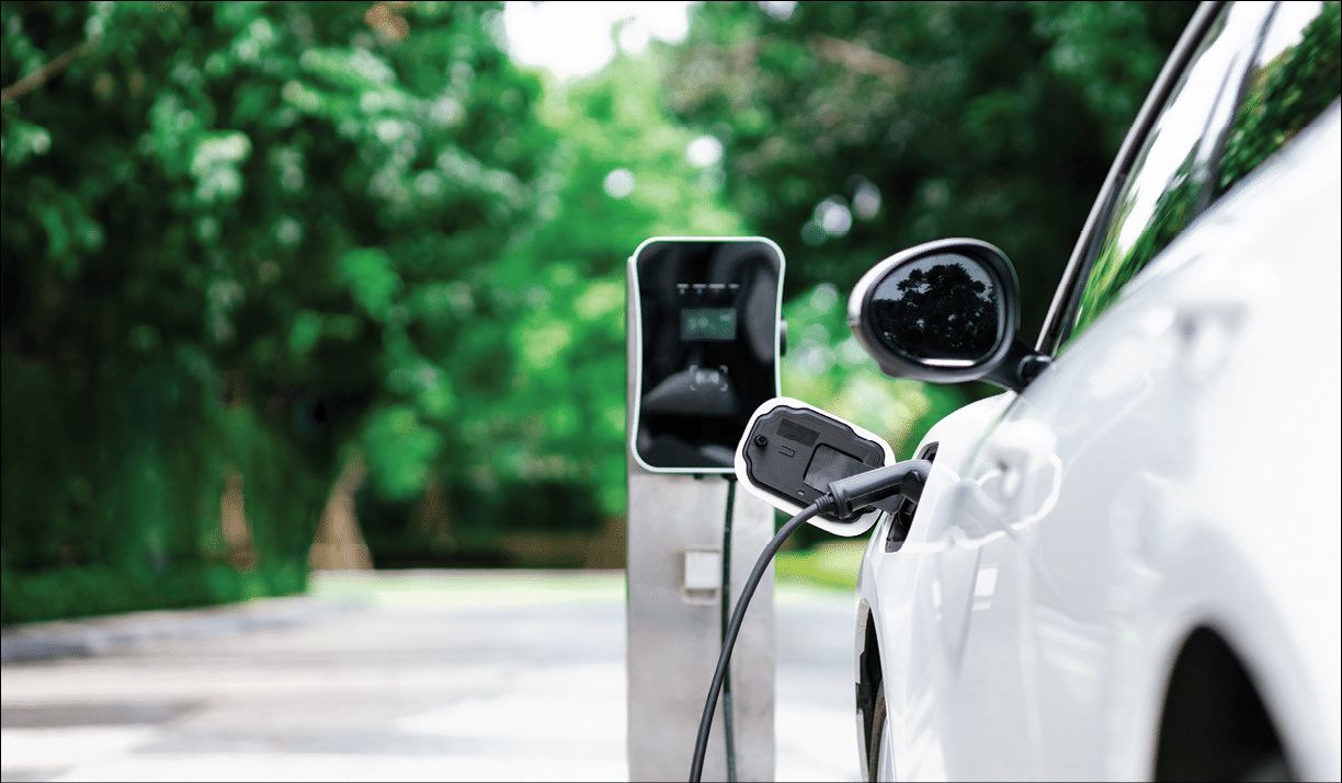 Focus closeup electric vehicle plugged in with EV charger device from blurred background of public charging station powered by renewable clean energy for progressive eco-friendly car concept.