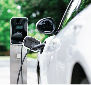 Focus closeup electric vehicle plugged in with EV charger device from blurred background of public charging station powered by renewable clean energy for progressive eco-friendly car concept.